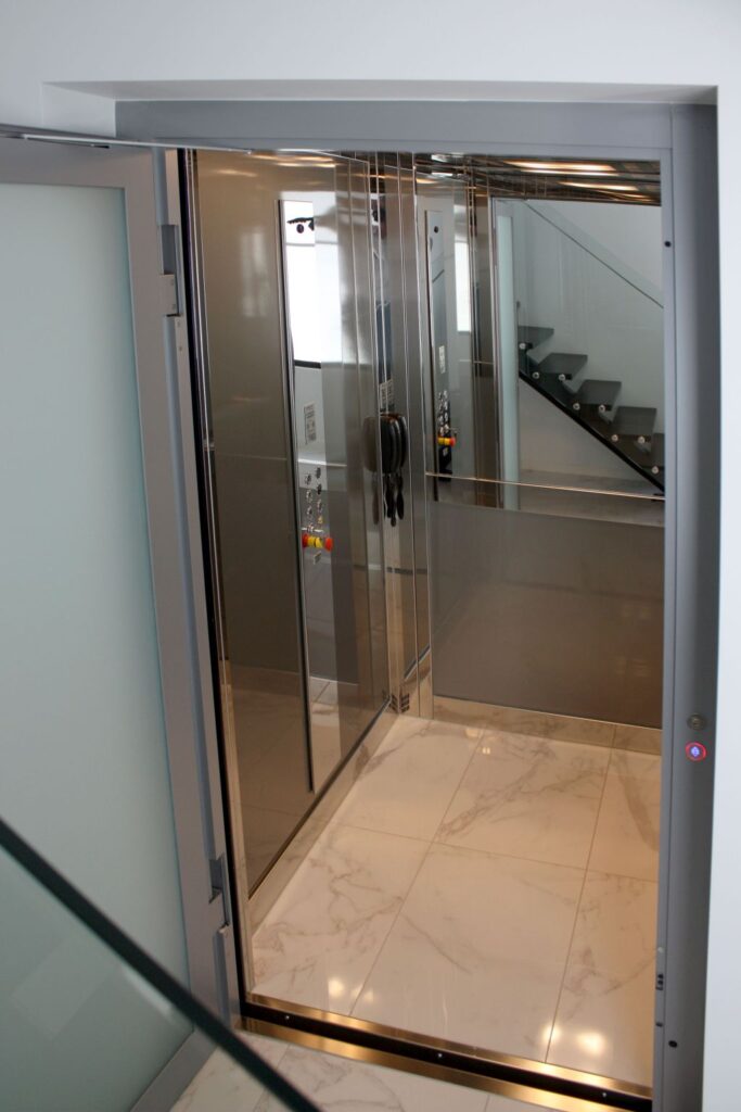 The open E1 lift car with a marble-look tiled floor and mirrored stainless walls, seen from the hallway of the Red Hill home