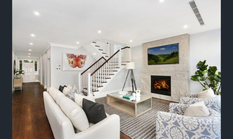 Living room with a white sofa, fireplace and staircase in the Rose Bay home