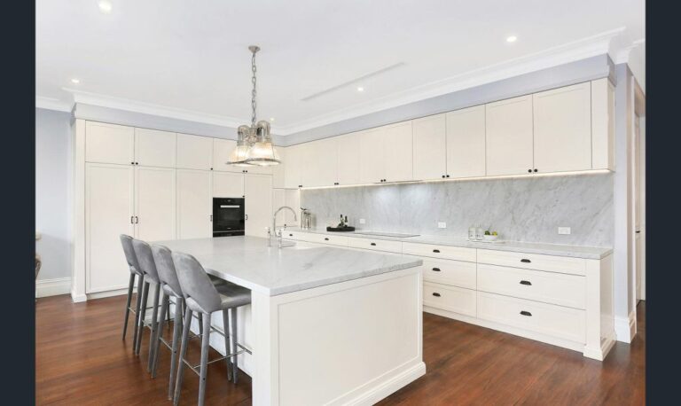 White kitchen with an island, bar stools and a pendant light on timber floors in the Rose Bay home