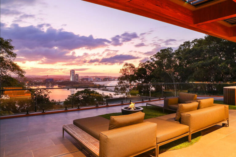 Outdoor lounge with a fire pit at sunset overlooking trees, a river and the Gold Coast skyline