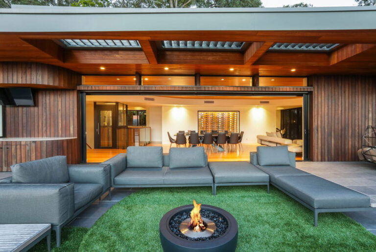 Outdoor lounge with a fire pit on artificial grass, looking through the open doors to the glass home lift beyond the dining room