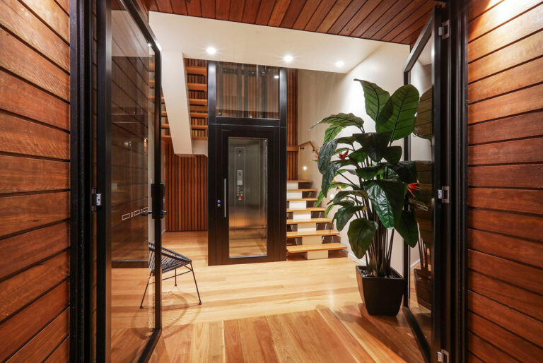 Glass home lift in a timber clad stairwell beside a large indoor plant in Currumbin