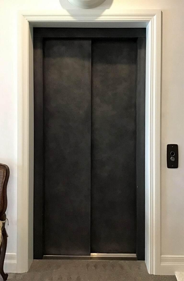 Closed dark velvet-finish lift doors with a call button in a white door frame