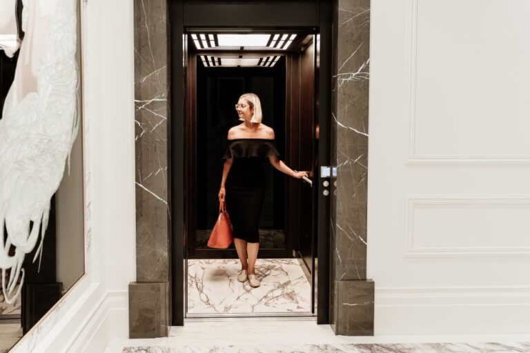 Woman stepping out of a lift framed by marble beside a white panelled wall, Leura Grove