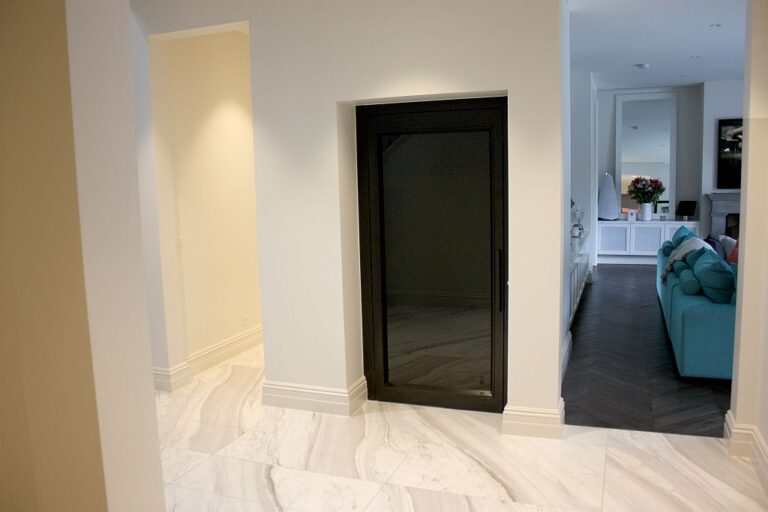 Black framed glass lift door in a white hallway with a stone tile floor in Melbourne