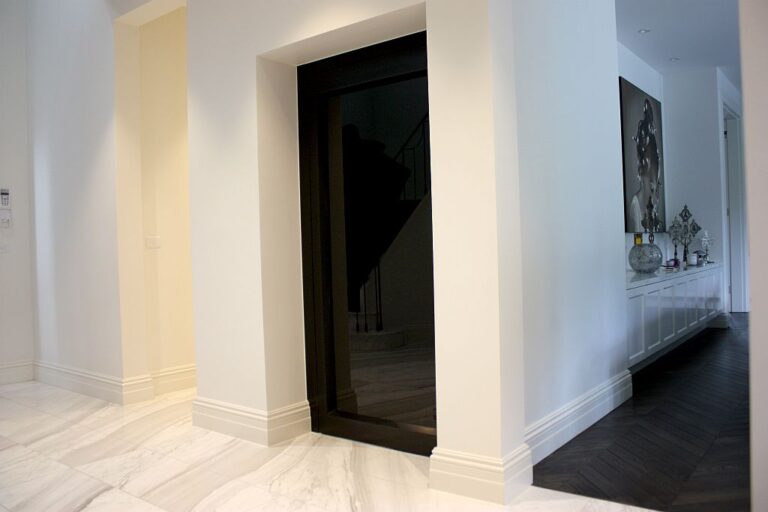 Black glass lift door set in a white hall with a marble look floor