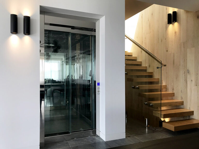 Dark glass lift doors beside a timber-clad stair wall and glass balustrade