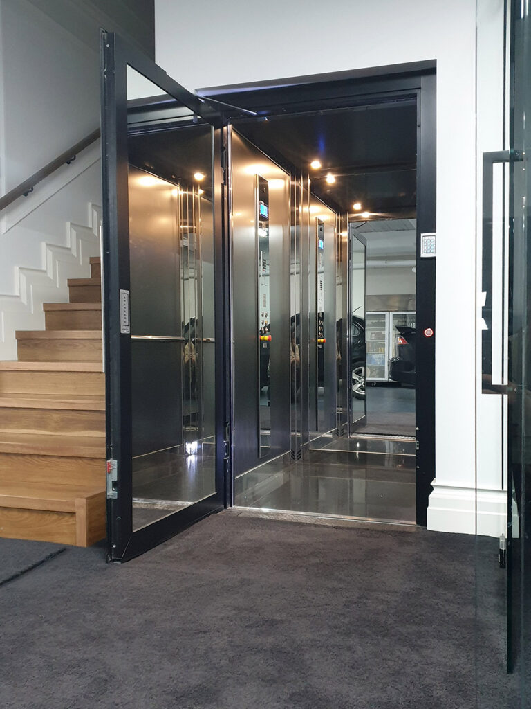 Open black-framed swing door E1 home lift beside a timber staircase in the Eaglemont home