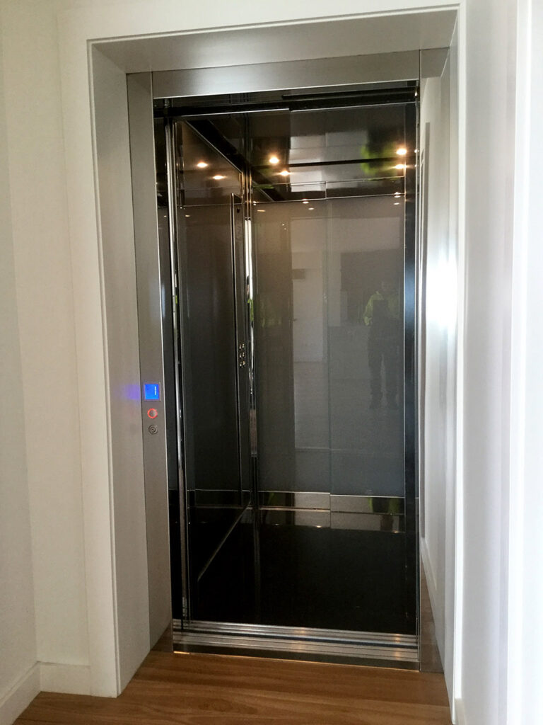 Inside the E2 lift cabin with dark glass walls, polished stainless trim and LED downlights