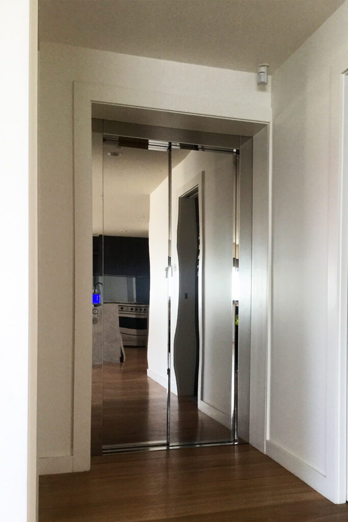 Polished stainless sliding lift doors at the end of a white hallway with a timber floor in a Fairlight home
