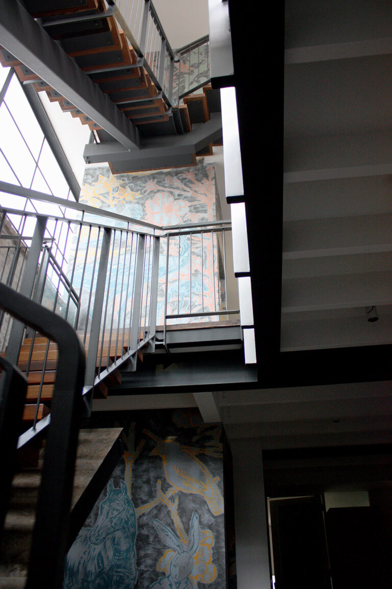 Black steel staircase with open timber treads rising past a hand-painted owl and dragonfly mural in the Collingwood home