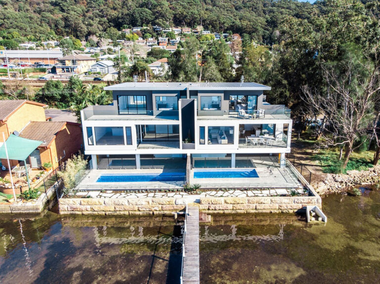 Aerial view of the waterfront home with two pools and a jetty