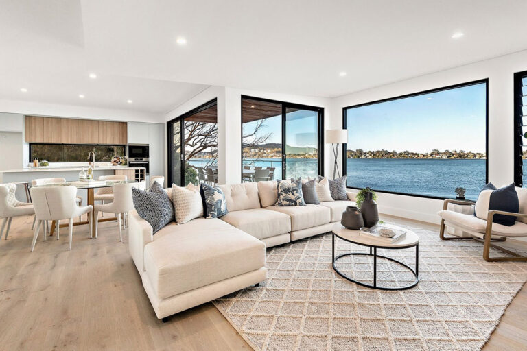 Open-plan living and dining area with a cream sofa and large water-view windows