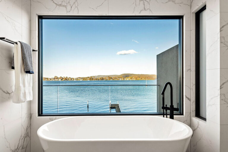 Freestanding bath beneath a large window overlooking the water