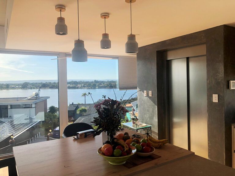 Dining table with a river view and pendant lights beside a lift in a dark surround