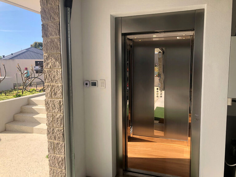 Lift open at the rendered entry with a mirrored cabin, a stone wall and steps outside
