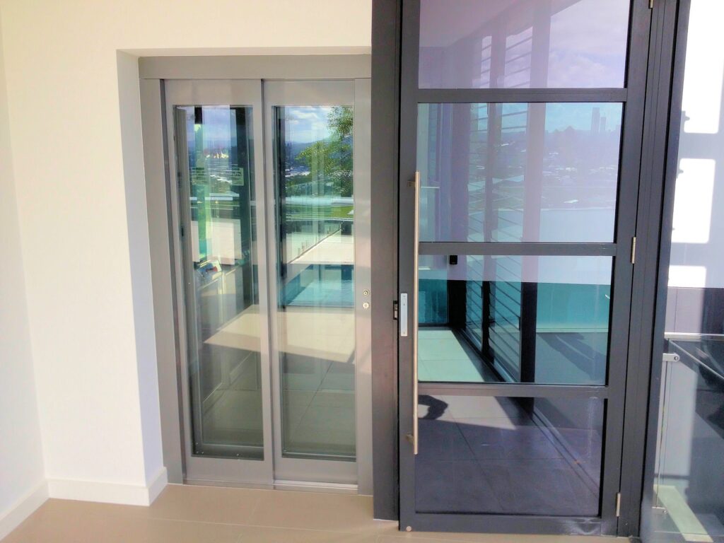 ElfoLift 2 glass landing doors set into the wall beside a glass entry door with city views