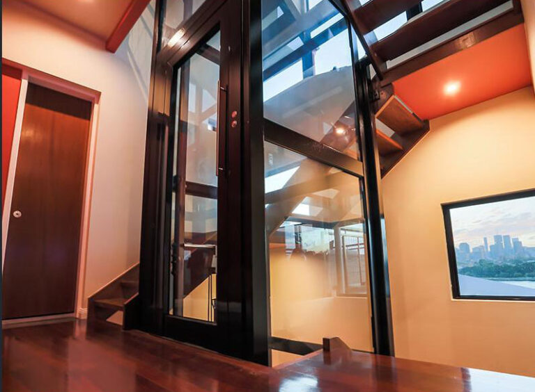 Glass lift in a stairwell with a city skyline in a window at right