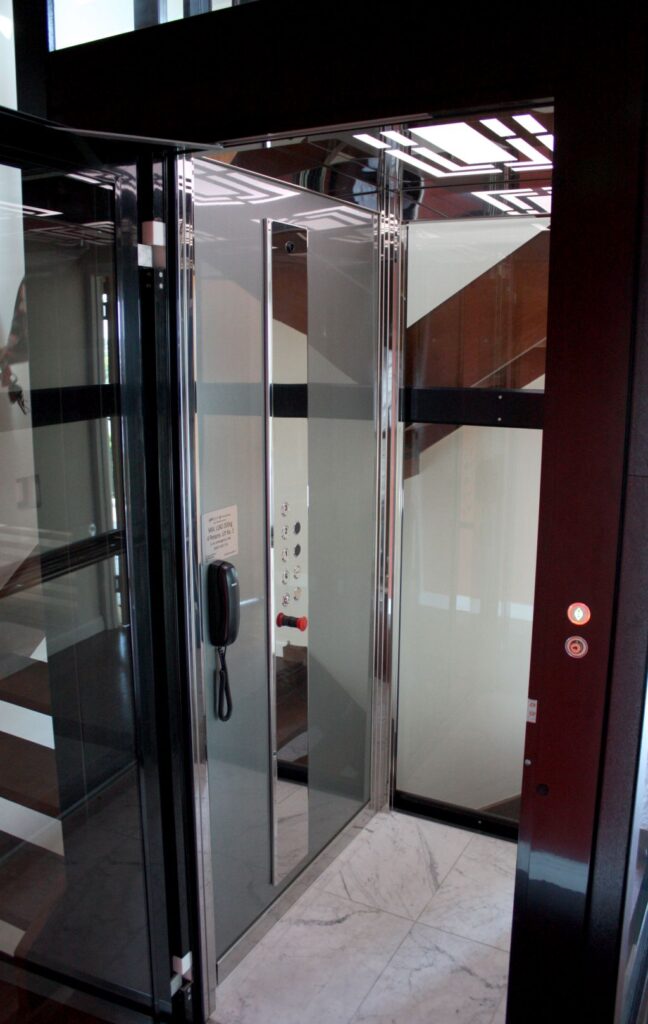 Inside the E1 cabin: a stainless steel control panel and phone, glass walls and marble floor tile