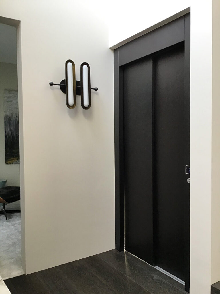Black timber-look lift doors beside a decorative bronze wall light in a Bellevue Hill hallway