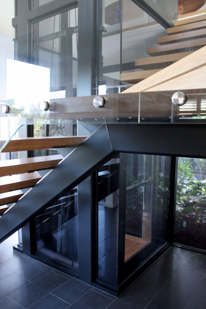 Base of the black lift shaft beside steel and timber stairs on dark floor tiles