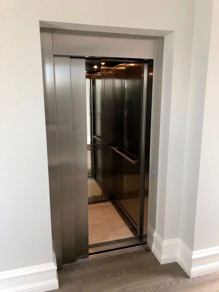 Open brushed stainless steel sliding lift door showing a cabin with a handrail and timber floor