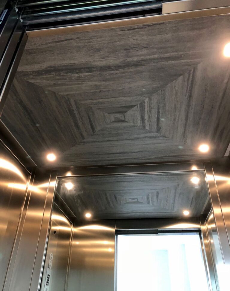 Looking up at a custom dark stone-look ceiling with downlights inside the lift cabin