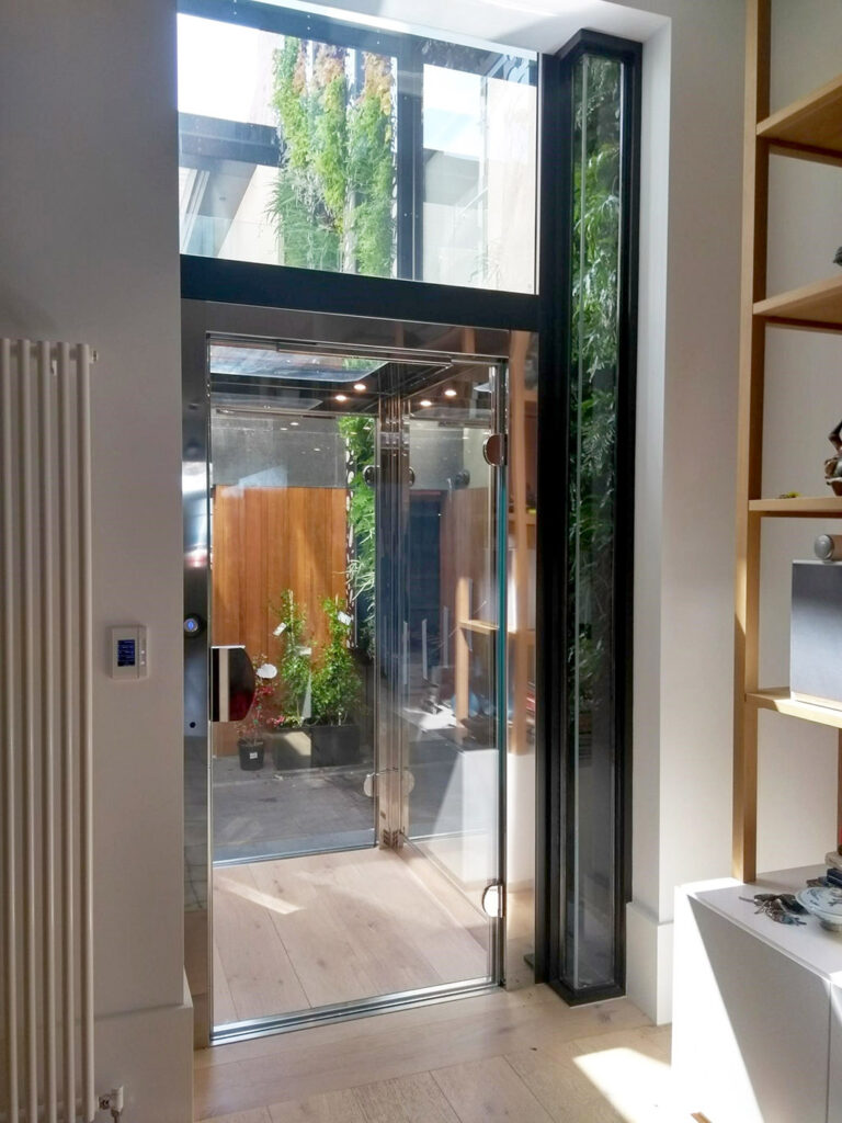 Lift with a polished steel door beside a tall green plant wall and shelving