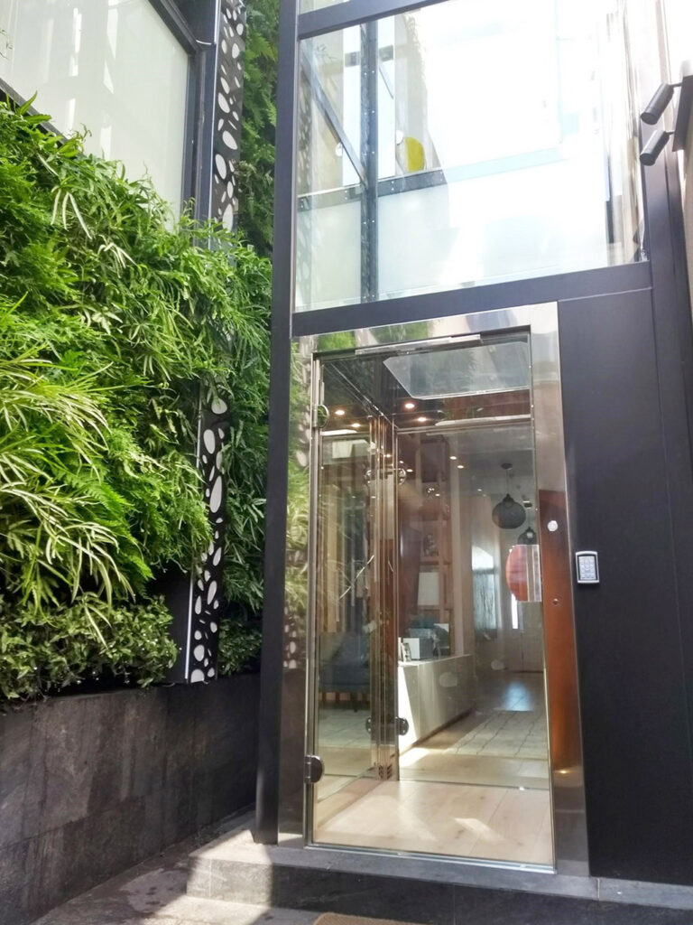 Steel and glass lift door at the base of a plant wall and glass shaft