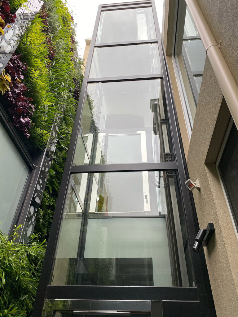 Glass lift shaft beside a living wall of green plants in an Albert Park home