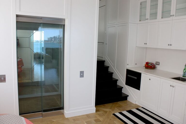 Glass lift door with a geometric pattern beside white cabinets and a black staircase