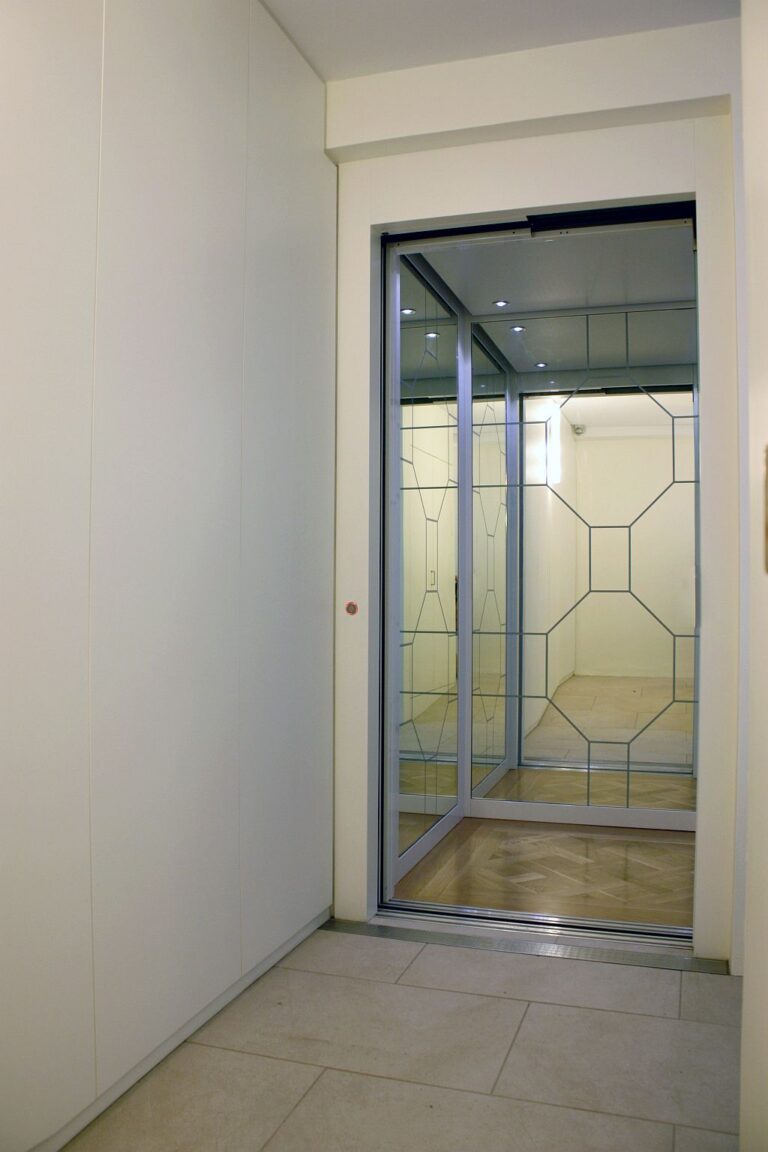 Glass lift entry on a tiled landing with a geometric pattern on the wall inside