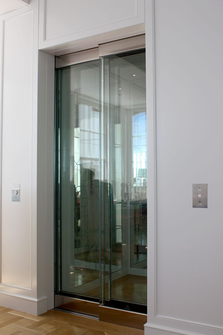 Glass lift door in a white surround with the outside view reflected in the glass