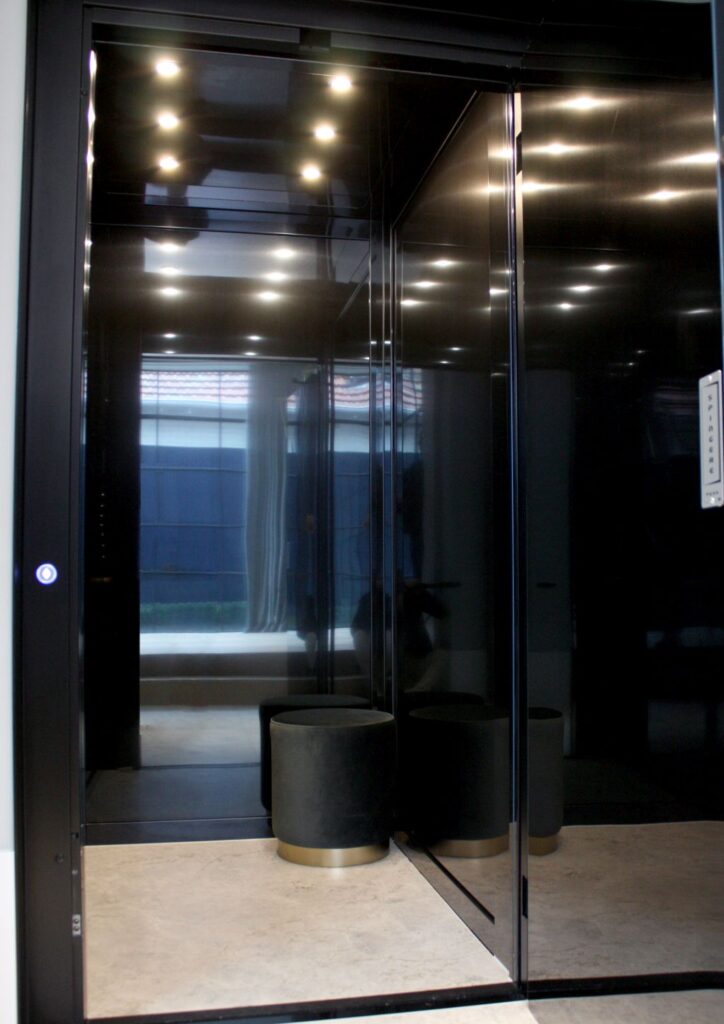 Inside the black stainless steel lift cabin, with mirror-finish walls and ceiling downlights reflecting the window beyond