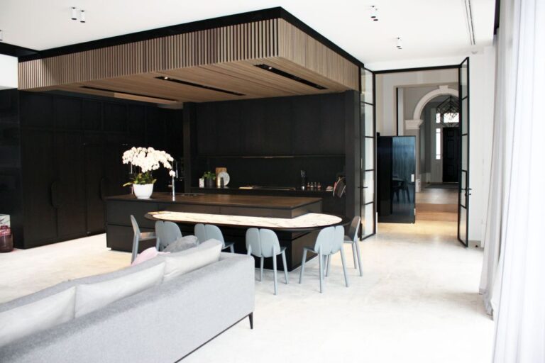 Open plan kitchen and living area with a timber slat ceiling and black joinery, with the black lift door beyond
