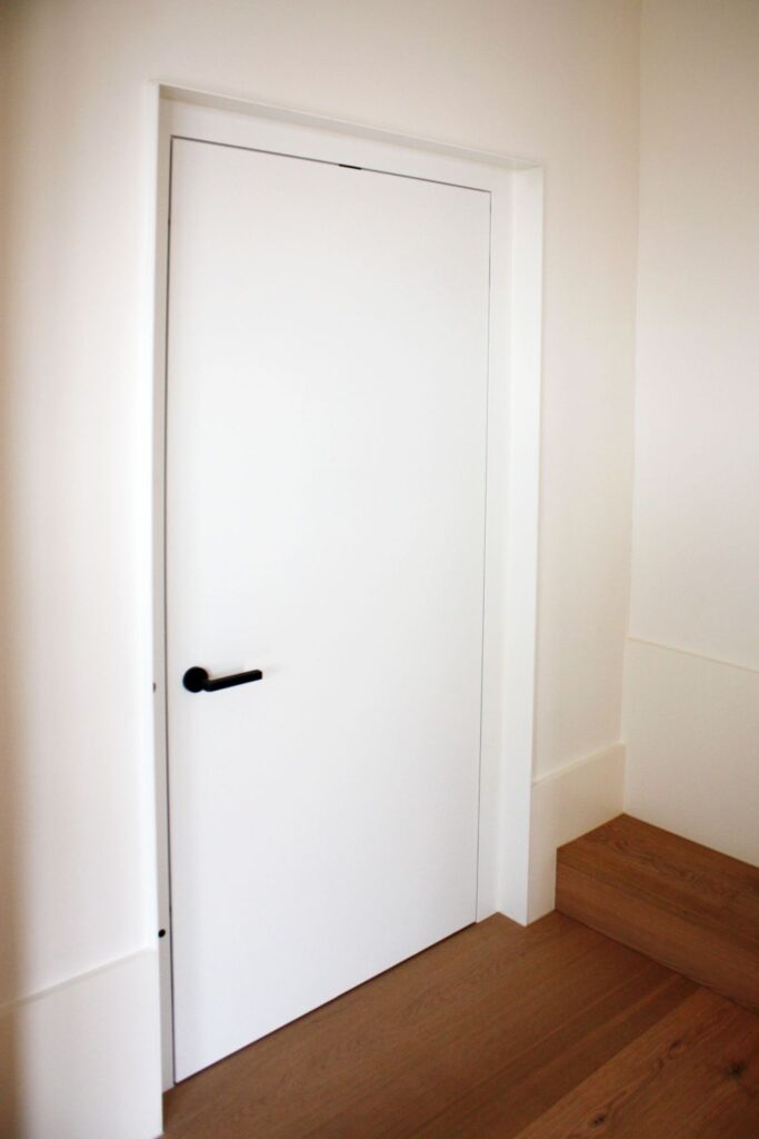 Closed white powdercoated lift door with a black lever handle set in an upper floor hallway wall