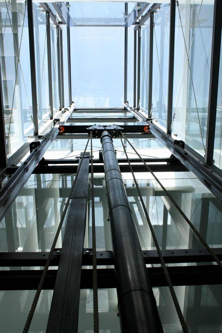 The guide rails and drive of the glass lift seen from below, with open sky above the shaft