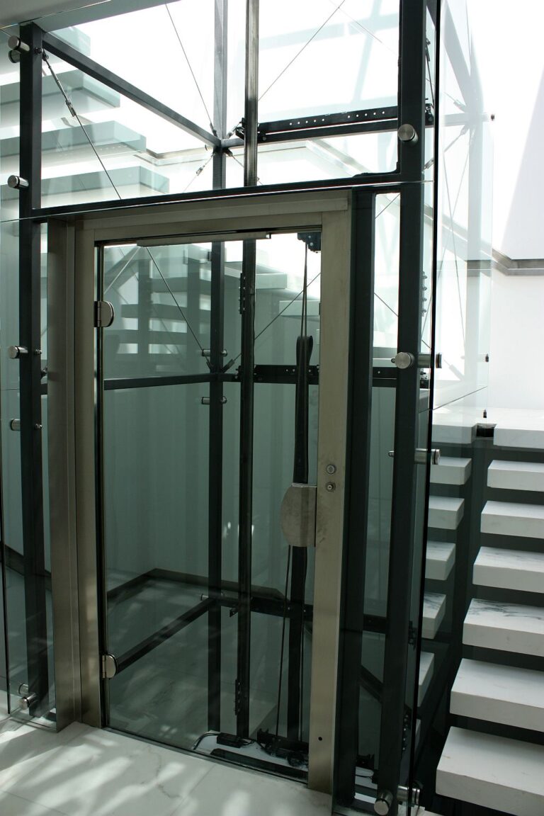 Glass lift landing door with a stainless steel frame beside a white floating staircase in McMahons Point