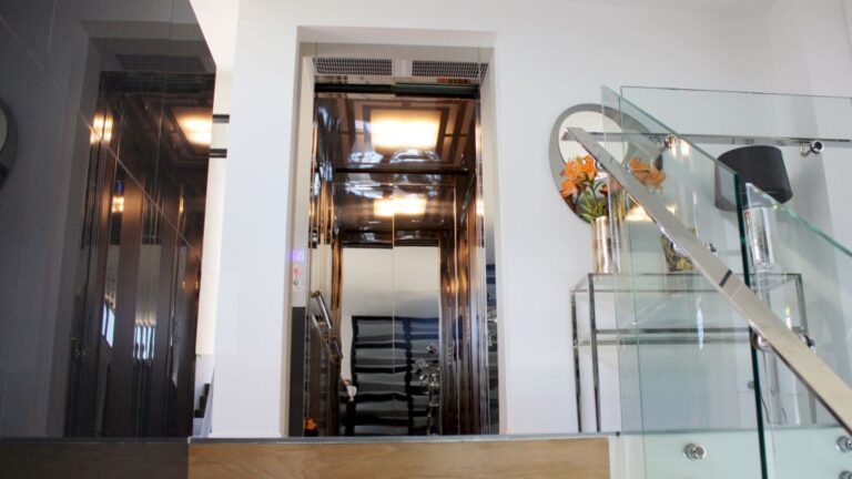 Glass-fronted home lift seen beyond a glass balustrade and staircase in Hamilton