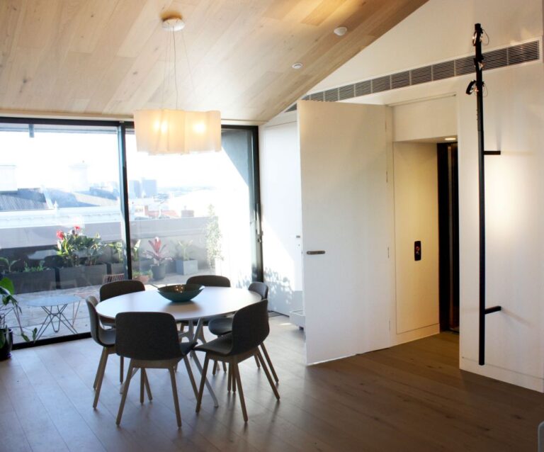 White flush door with a tall black handle beside a dining table and glass wall