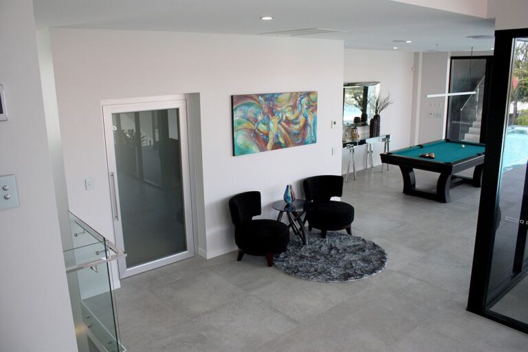 Living area with a frosted glass lift door beside a pool table and black armchairs