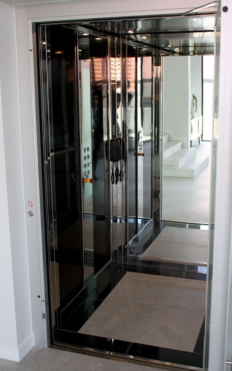 Inside the E1 lift car with high-gloss dark wall panels, a mirror and a tiled floor with a border