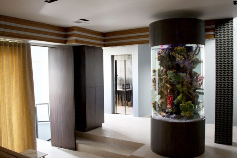 Living space in the Hollywood Hills home with a round aquarium column and the mirrored lift doors in the background