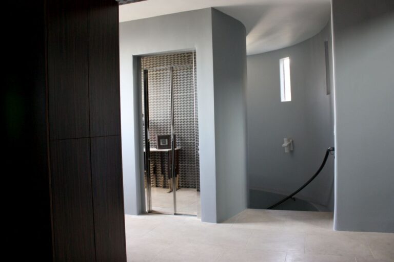 Lift door in a curved grey stairwell with a narrow vertical window