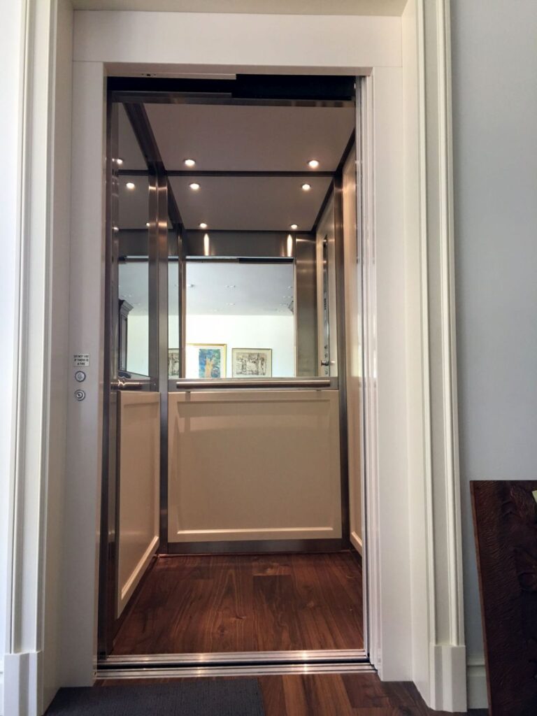 Front view of the open lift cabin with a mirror, downlights and a timber floor