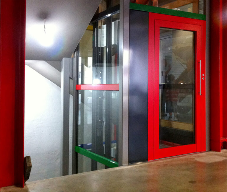 Lift with a bright red door and frame beside a stairwell in a Carlton home