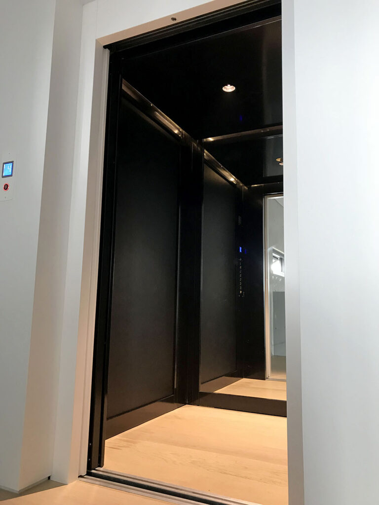 Open lift door showing the black cabin interior, mirrored rear wall and timber floor in a Maroubra home