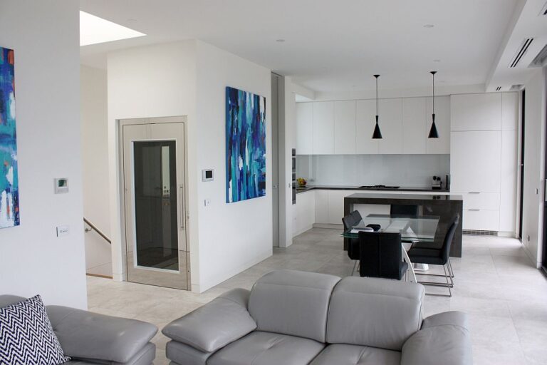 Open plan living and kitchen area with a glass panelled lift door beside a blue painting