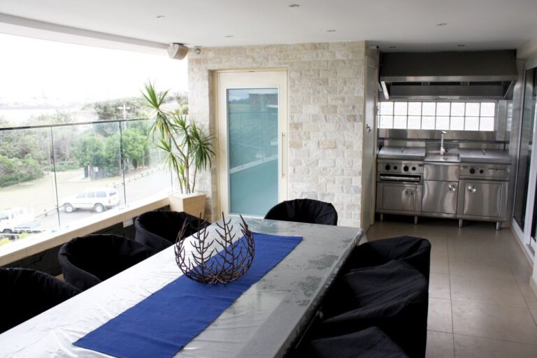 Dining table with a blue runner and black chairs beside a stone-clad wall and frosted door