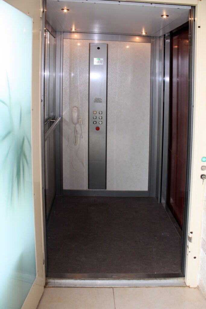 Inside the lift cabin with stainless steel panels, a button strip and a dark floor
